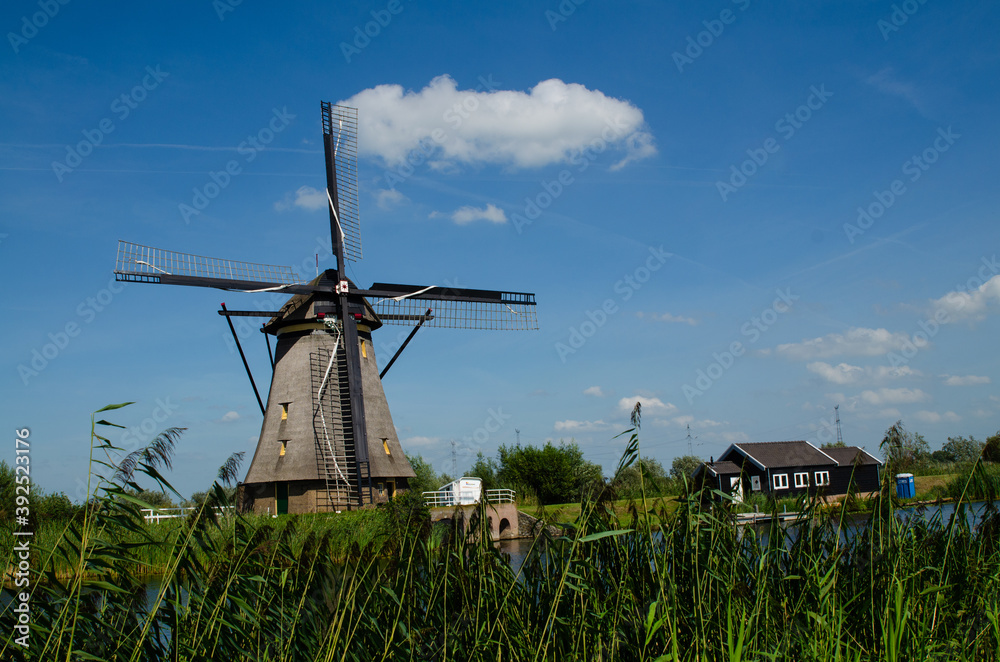 Kinderdijk, The Netherlands, August 2019. On a beautiful summer day a historic windmill, in perfect condition, in the Dutch countryside furrowed by canals lined with tall green grasses. Kinderdijk, The Netherlands, August 2019. On a beautiful summer day a historic windmill, in perfect condition, in the Dutch countryside furrowed by canals lined with tall green grasses.