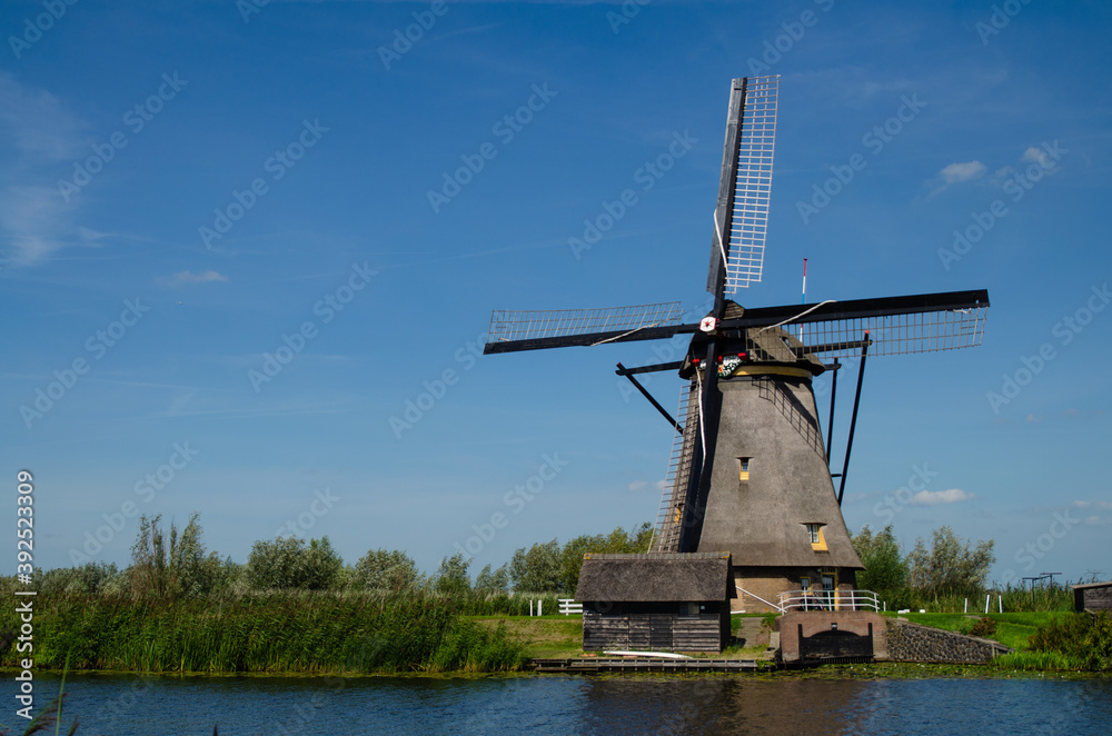 Kinderdijk, The Netherlands, August 2019. On a beautiful summer day a historic windmill, in perfect condition, in the Dutch countryside furrowed by canals lined with tall green grasses.