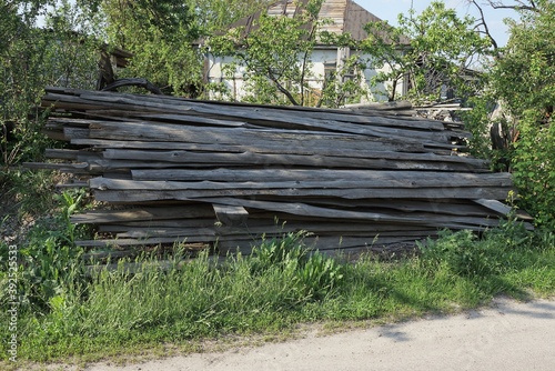 Fototapeta Naklejka Na Ścianę i Meble -  a large pile of gray wooden boards in green grass on the street