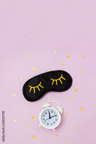 Fotografie Female sleep mask, alarm clock and starry confetti on pink background