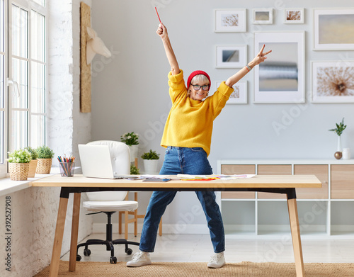 cheerful elderly woman freelancer creative designer in a red hat having fun and dancing in workplace. photo