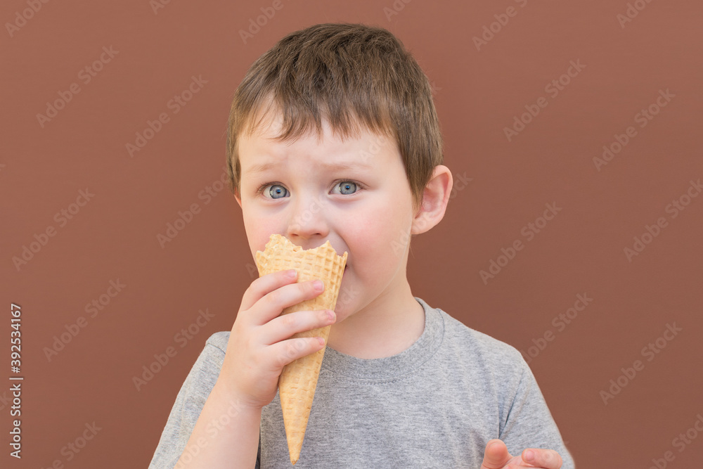 Caucasian boy, funny and cute eating a waffle cone on a brown background. horizontal photo close-up. Caucasian boy, funny and cute eating a waffle cone on a brown background. horizontal photo close-up.