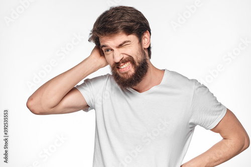 cheerful bearded man in a white t-shirt emotions gestures with his hands light background studio