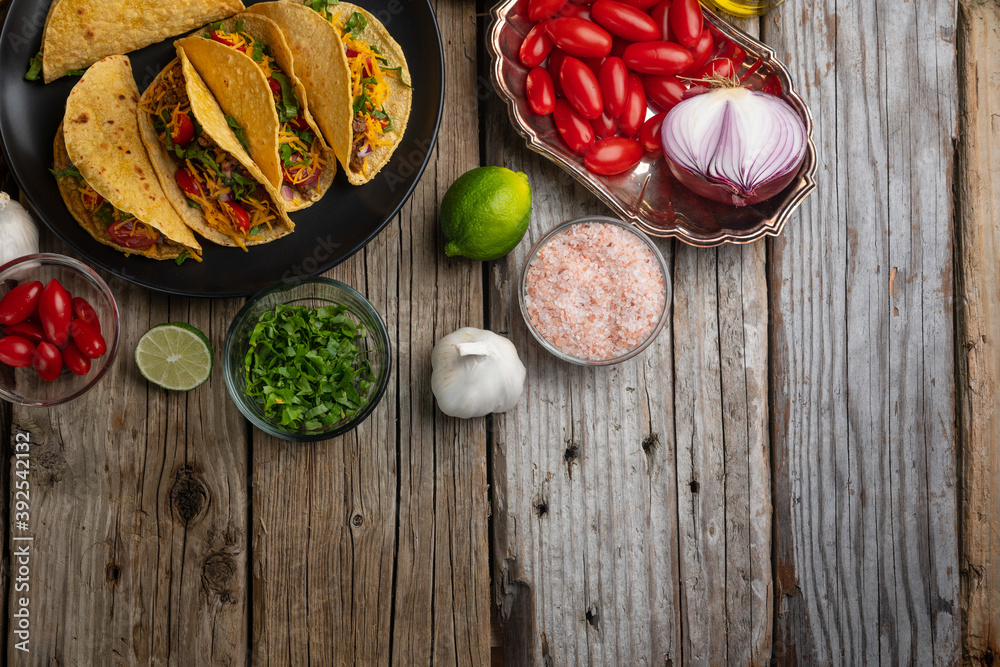 Top view of plate with tasty mexican tacos on rustic wooden table with variety ingredients background. Concept of traditional food. View from above. Flat lay. Space for text.