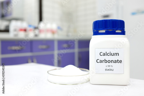 Selective focus of a bottle of calcium carbonate chemical compound or soda ash beside a petri dish with solid crystalline powder substance. White Chemistry laboratory background with copy space.
