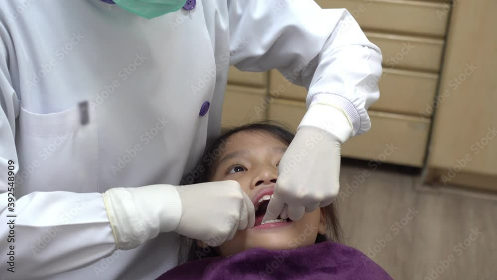 dentist using dental floss to clean food from tooth of asian girl dentist using dental floss to clean food from tooth of asian girl