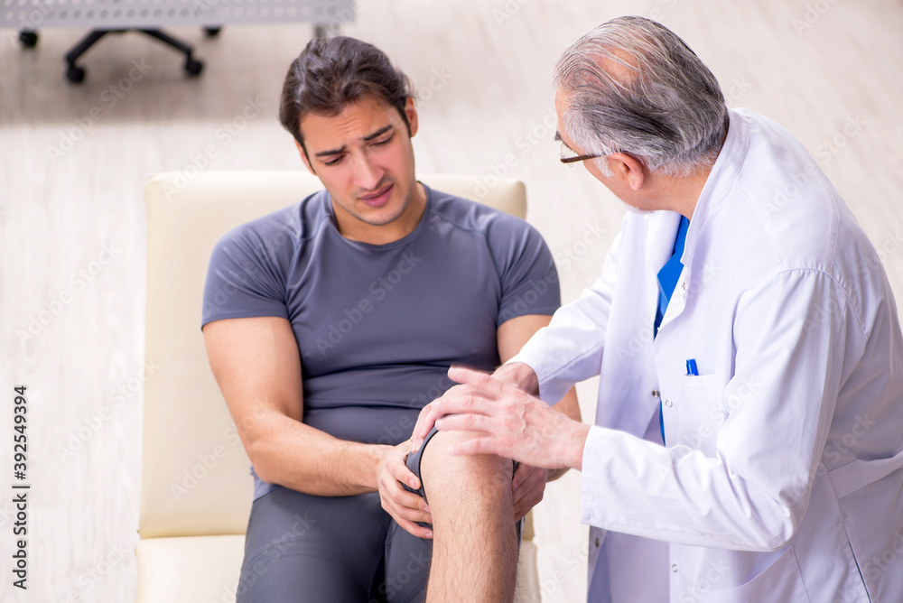Young male patient visiting old doctor traumatologist Young male patient visiting old doctor traumatologist