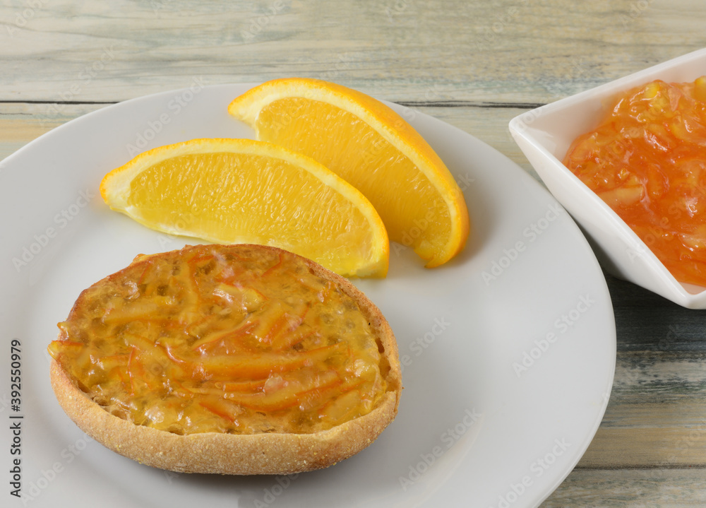 Orange marmalade on toasted whole wheat toast with orange slices and marmalade in condiment bowl Orange marmalade on toasted whole wheat toast with orange slices and marmalade in condiment bowl