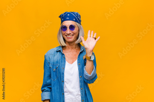 middle age woman smiling happily and cheerfully, waving hand, welcoming and greeting you, or saying goodbye