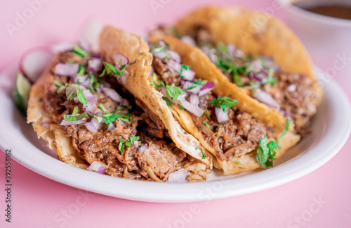 Delicious tacos of birria on a white plate with a broth in the back.