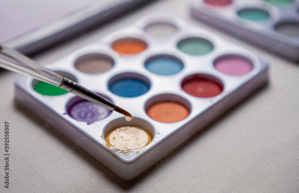 Naklejka premium Colored watercolors on a table and up a brush with water dripping in close up concept.