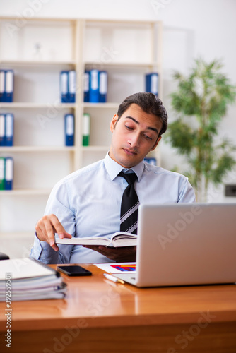 Young male student employee reading book at workplace