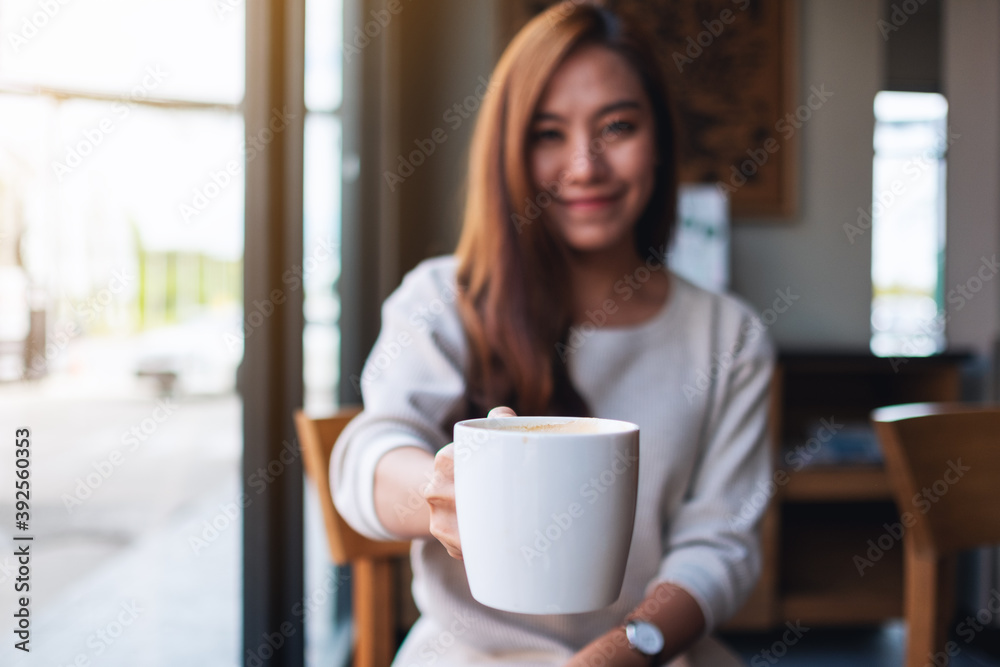 Closeup image of a beautiful young asian woman holding and giving a cup of hot coffee in cafe Closeup image of a beautiful young asian woman holding and giving a cup of hot coffee in cafe