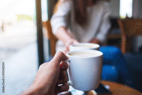 Closeup image of man and woman clinking white coffee mugs in cafe