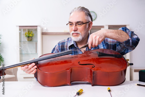 Fotografie Senior male repairman repairing musical instruments at home