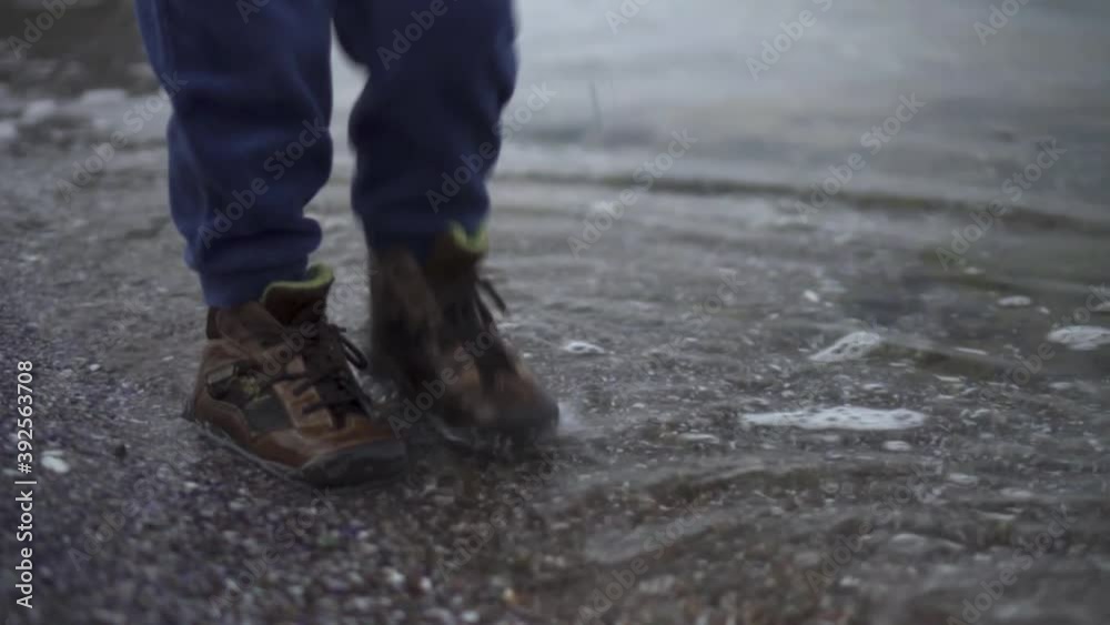 Playful Kid In Shoes Stomping Feet On The Shore - Closeup Shot Playful Kid In Shoes Stomping Feet On The Shore - Closeup Shot