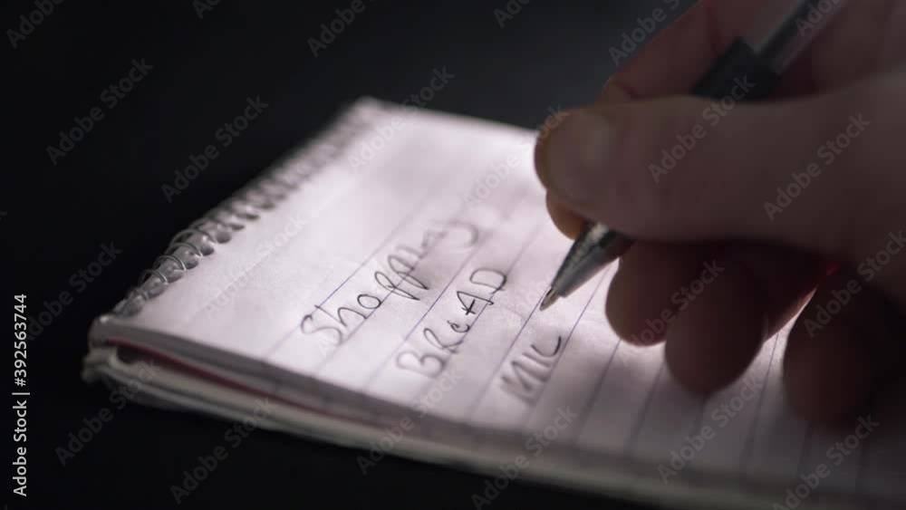 Hand writing shopping list on notepad for essentials close up shot Hand writing shopping list on notepad for essentials close up shot