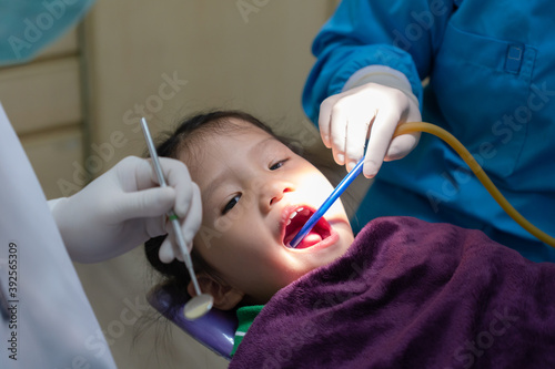young dentist and dental assiatant doing procedure to treat dental caries fot girl in clinic