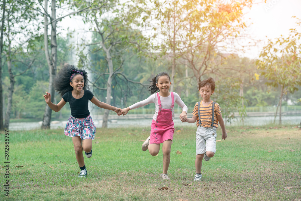 Group of young children happily  holding hands and running towards camera in park.