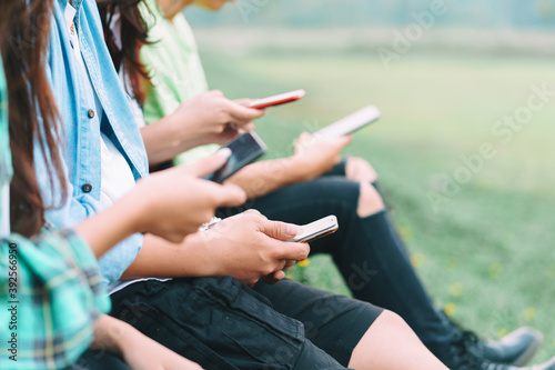A cropped image of A group Asian friends are sitting using their smartphones and chatting in the park