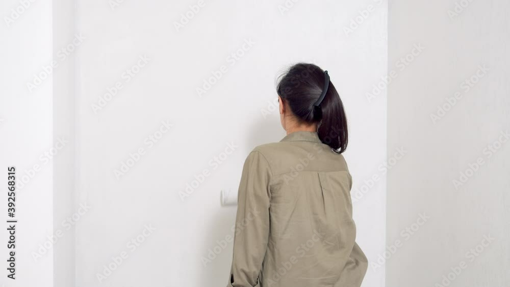 Young woman painting the wall with a roller. View from the back. Do-it-yourself renovation and new housing concept. Copy space. Young woman painting the wall with a roller. View from the back. Do-it-yourself renovation and new housing concept. Copy space.