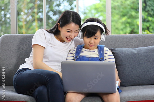 Asian mother teaching her daughter to learn from online class using laptop for homeschooling and education concept