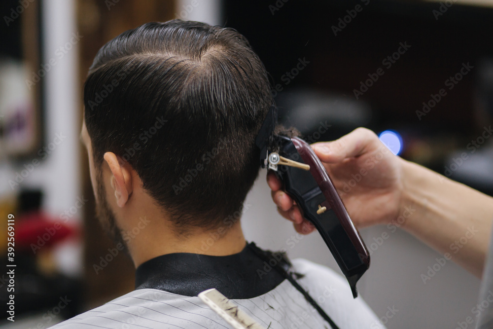 Back view of Men in beauty salon. Men's haircut in a barbershop. New haircut style 2021. Professional hairdresser uses a hair clipper for fringing hair