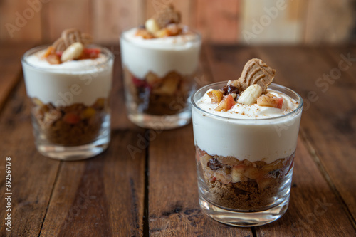 Kuchen im Glas mit St  cken vom Bratapfel  Zimt  Spekulatius  Apfel  Mandeln und Rosinen mit einer Creme aus Quark oder Mascarpone auf einem Tisch aus Holz in einer gem  tlichen K  che zu Weihnachten