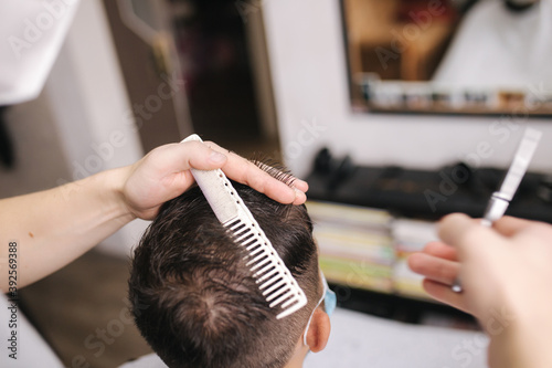 Man getting hair cut by scissor in barbershop. Barber use scissor and wearing mask during coronavirus pandemic. Professional barber work at home. Covid-19 quarantine