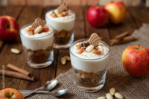 Kuchen im Glas mit Stücken vom Bratapfel, Zimt, Spekulatius, Apfel, Mandeln und Rosinen mit einer Creme aus Quark oder Mascarpone auf einem Tisch aus Holz in einer gemütlichen Küche zu Weihnachten