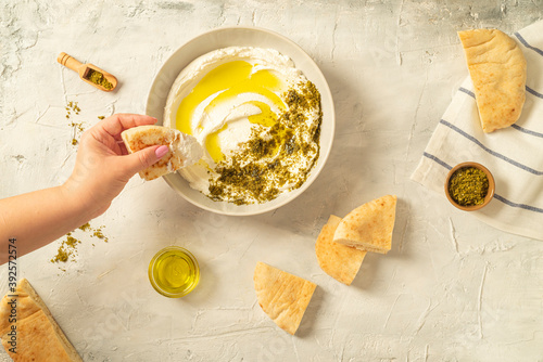 Popular middle eastern appetizer labneh or labaneh, soft white goat milk cheese with olive oil, hyssop or zaatar, served with pita bread over grey table, flaylay.