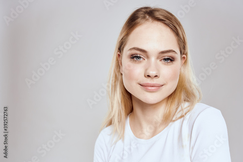 Cheerful blonde woman in white t-shirt cropped view light background