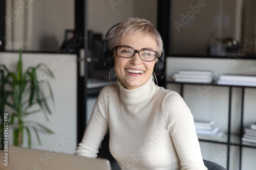Close up smiling businesswoman wearing headphones looking to aside, dreaming, visualizing good future, friendly happy female employee manager working online, consulting client, watching webinar