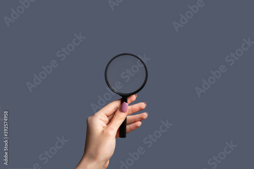 Advertising background. Search engine. Discovery research. Female hand exploring information with magnifying glass zoom isolated on purple empty space.