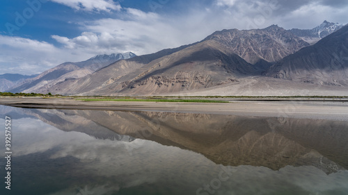 Panorama view of the Wakhan Corridor in the Tajikistan Pamir mountains looking towards the Hindu Kush range in Afghanistan with reflection into Panj river