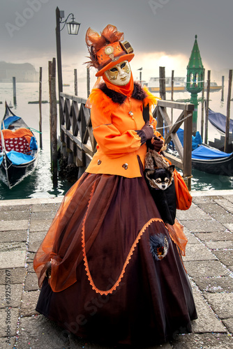 Pretty woman wearing ornate carnival costume with face hidden under mask and hat poses at San Marco square