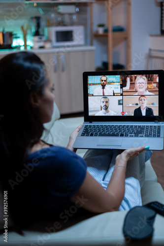 Back view of woman using laptop on videocall sitting on comfortable couch. Remote worker having online meeting consulting with colleagues on video conference and webcam chat using internet technology.