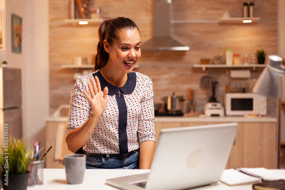 Businesswoman waving during video conference while working from home at night. Employee using modern technology at midnight doing overtime for job, business, career, network, lifestyle ,wireless. Businesswoman waving during video conference while working from home at night. Employee using modern technology at midnight doing overtime for job, business, career, network, lifestyle ,wireless.