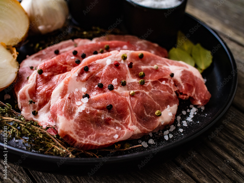 Raw pork chops with onion garlic and seasonings on plate on wooden table