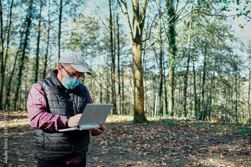 Mature man wearing mask working with laptop in field