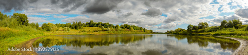 Summer panoramic landscape with calm river and beautiful clouds in blue sky