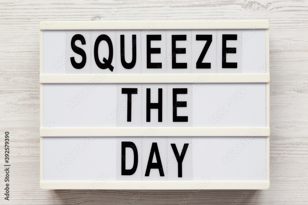'Squeeze the day' on a lightbox on a white wooden surface, overhead view. Flat lay, top view, from above.