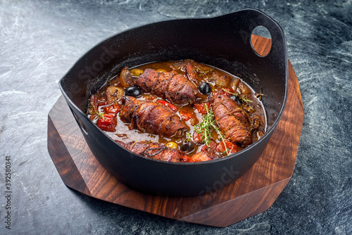 Modern style traditional slow cooked German beef roulades with vegetable and olives in spicy gravy sauce as close-up in a design pot