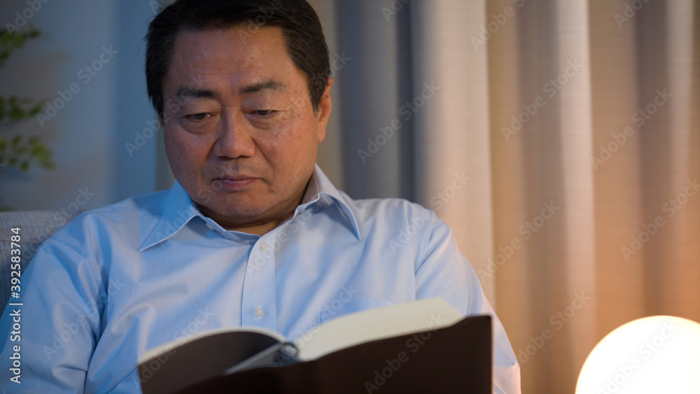 Fototapeta premium ソファーで本を読んでいる中年男性