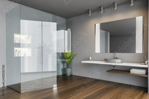 Grey bathroom with transparent shower cabin and sink with mirror on wooden floor