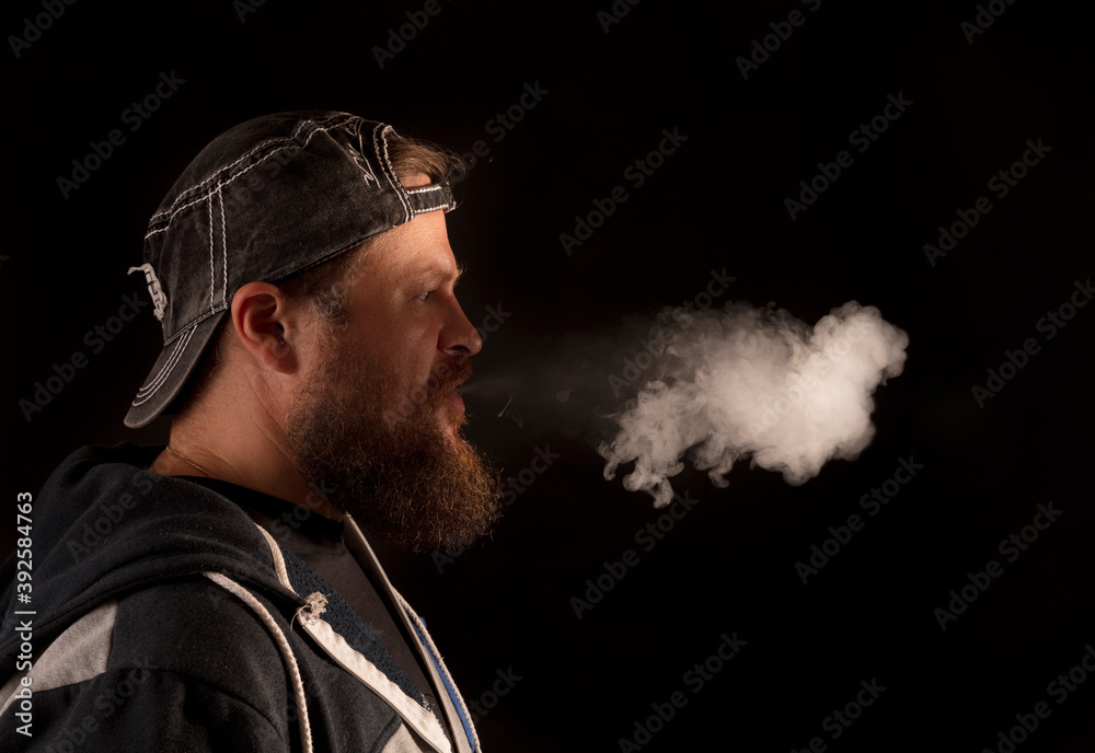Bearded man in cap and casual clothes exhaling vapour from his mouth