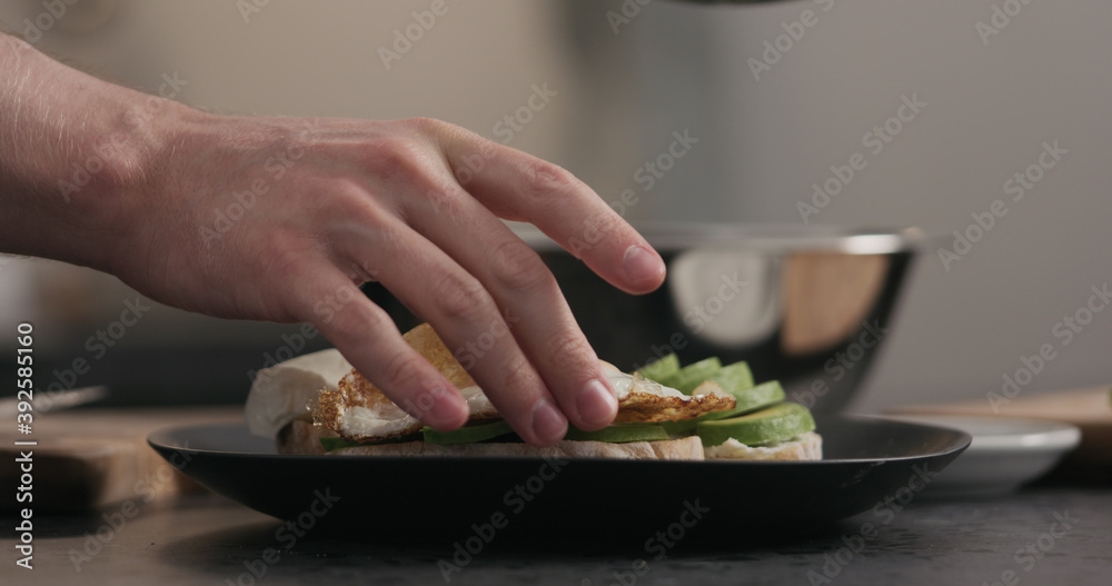 man makes sandwich with avocado and fried egg