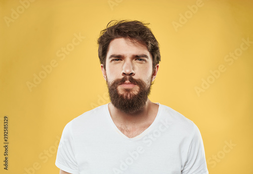 A man with a beard and mustache on a yellow background and a white T-shirt