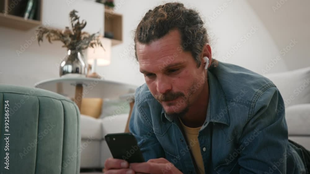 Someone's having a good time on their device. Male relaxing on the floor at home and using cellphone Someone's having a good time on their device. Male relaxing on the floor at home and using cellphone