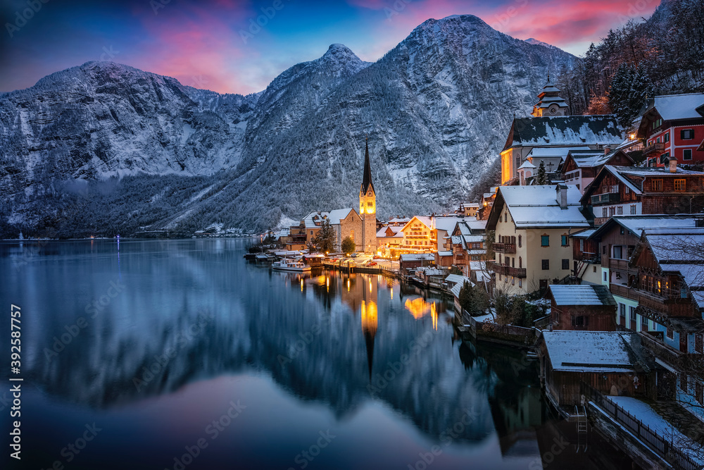 Obraz premium The little village of Hallstatt, Austria, during winter dusk time with snow, glowing sky in the mountains and warm lights from the houses